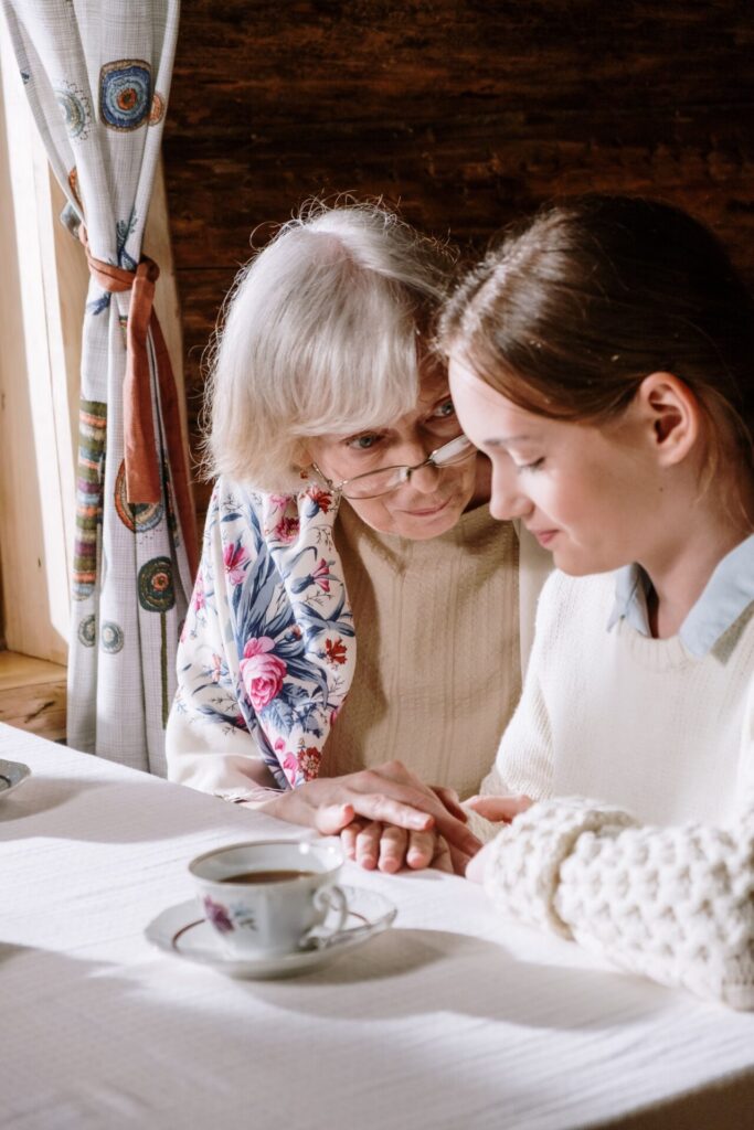 Senior and adult daughter holding hands during an end-of-life conversation at home.
